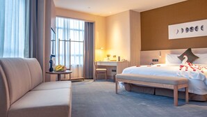 A modern hotel room with a large bed, a sofa, a desk, and a view of the city through large windows. - Shundi SHY Hotel Jinshan Lake Zhenjiang (Zhenjiang)