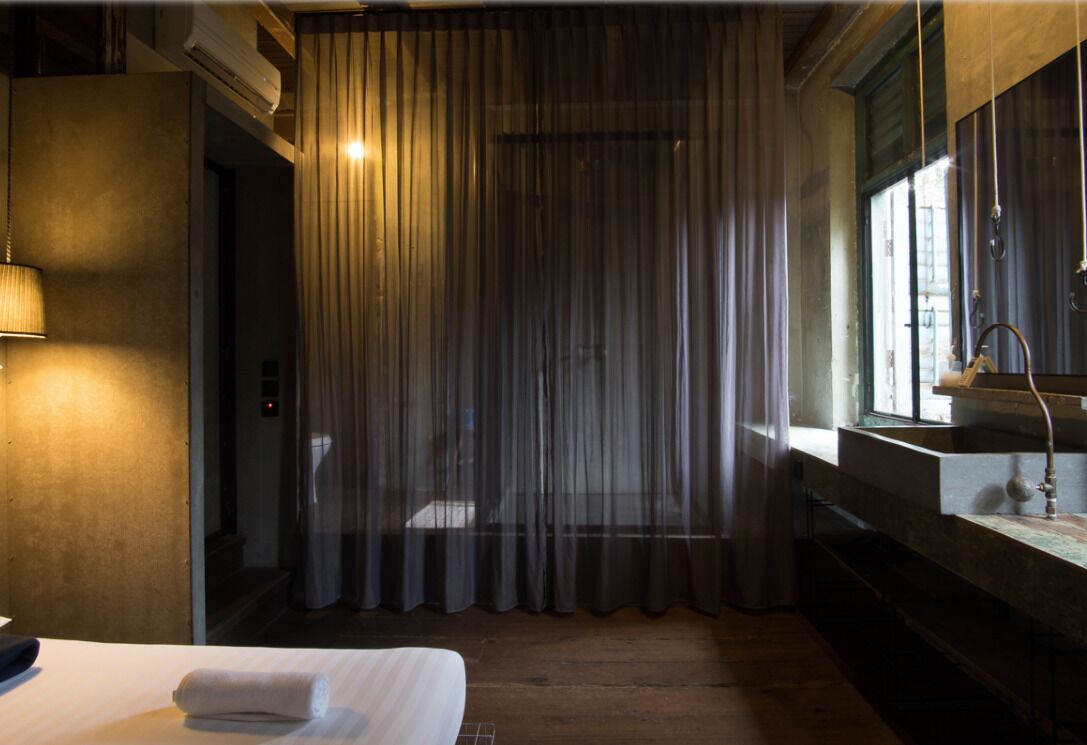 Habitación de hotel con cama, baño con lavamanos y espejo, y ventana con cortinas.
