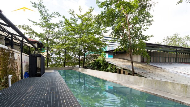 An outdoor swimming pool with a tiled deck, surrounded by trees and a building with a sloped roof. - Belakang Kong Heng by DreamScape (Ipoh)