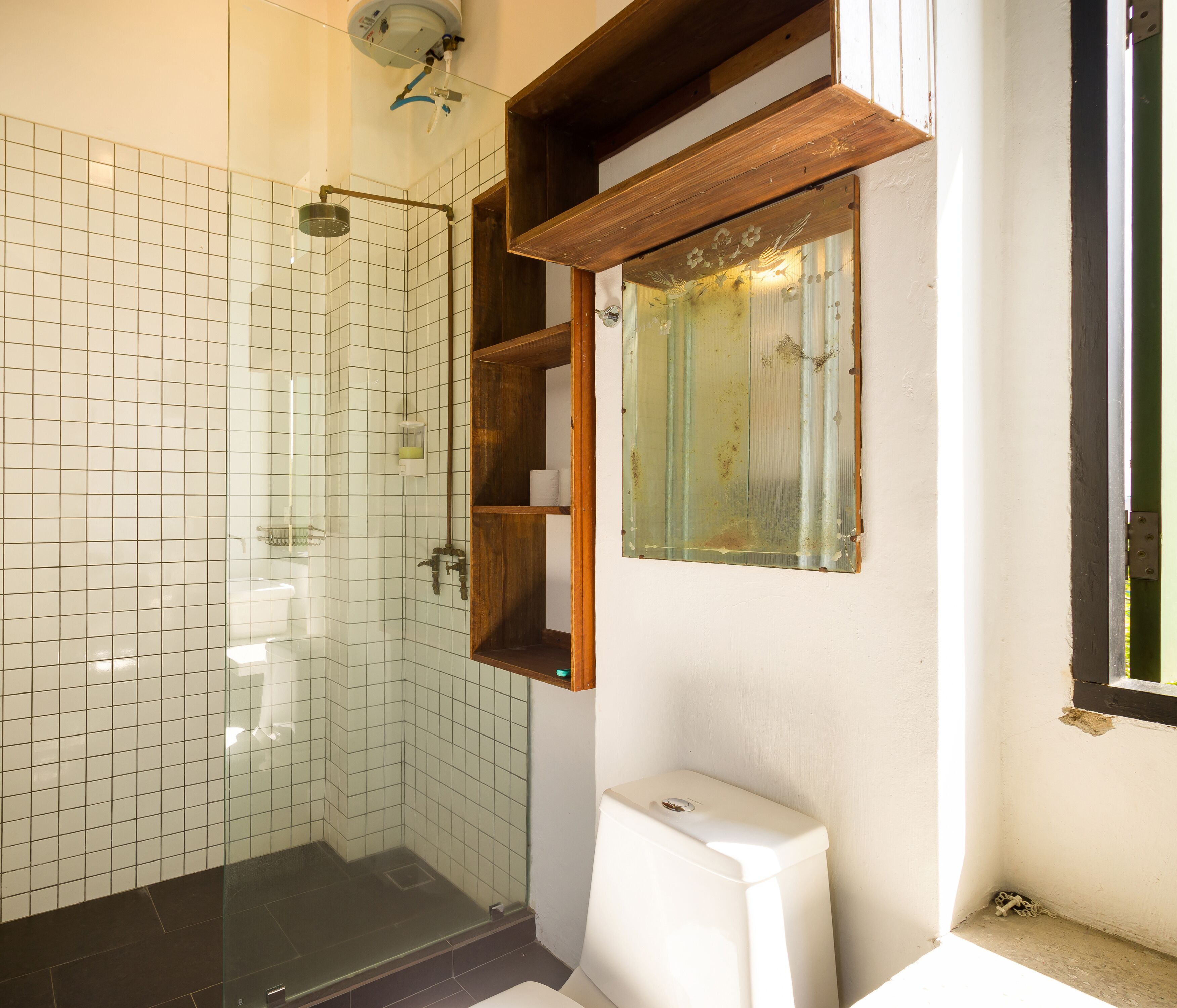 Un baño con cabina de ducha de vidrio, un inodoro blanco y un estante de madera con un espejo.