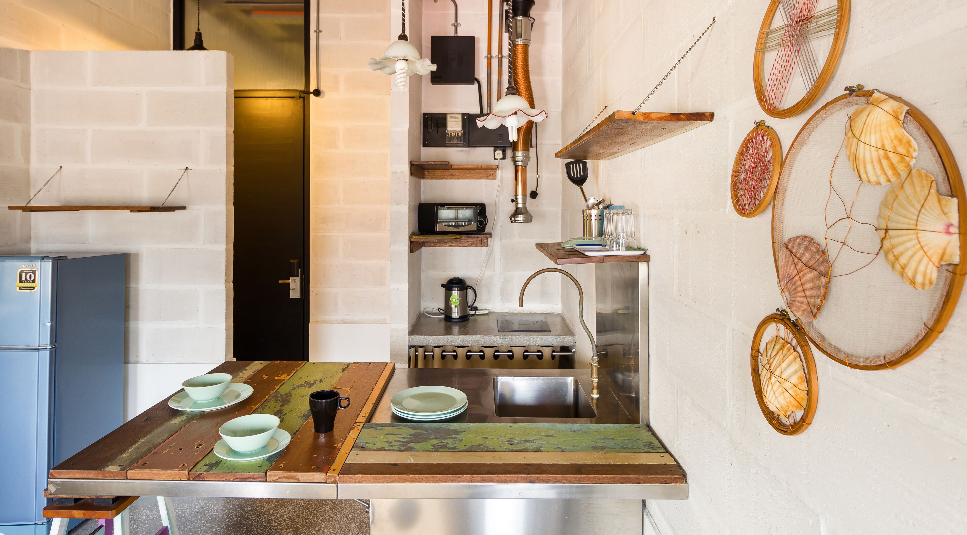 A kitchen with a rustic wooden countertop, a sink, and a stove. There are decorative shells on the wall and a small shelf with kitchen items.