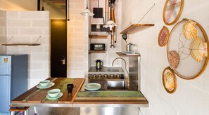 A kitchen with a rustic wooden countertop, a sink, and a stove. There are decorative shells on the wall and a small shelf with kitchen items. - Belakang Kong Heng by DreamScape (Ipoh)