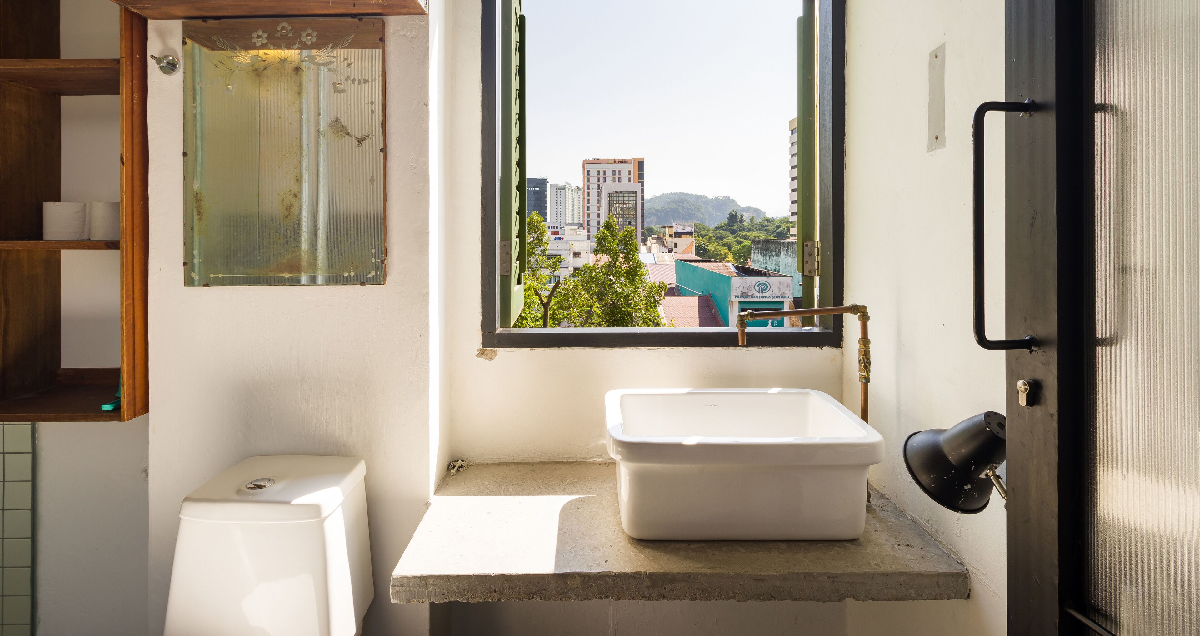 A small bathroom with a toilet, a sink, and a window with a view of buildings.