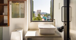 A small bathroom with a toilet, a sink, and a window with a view of buildings. - Belakang Kong Heng by DreamScape (Ipoh)