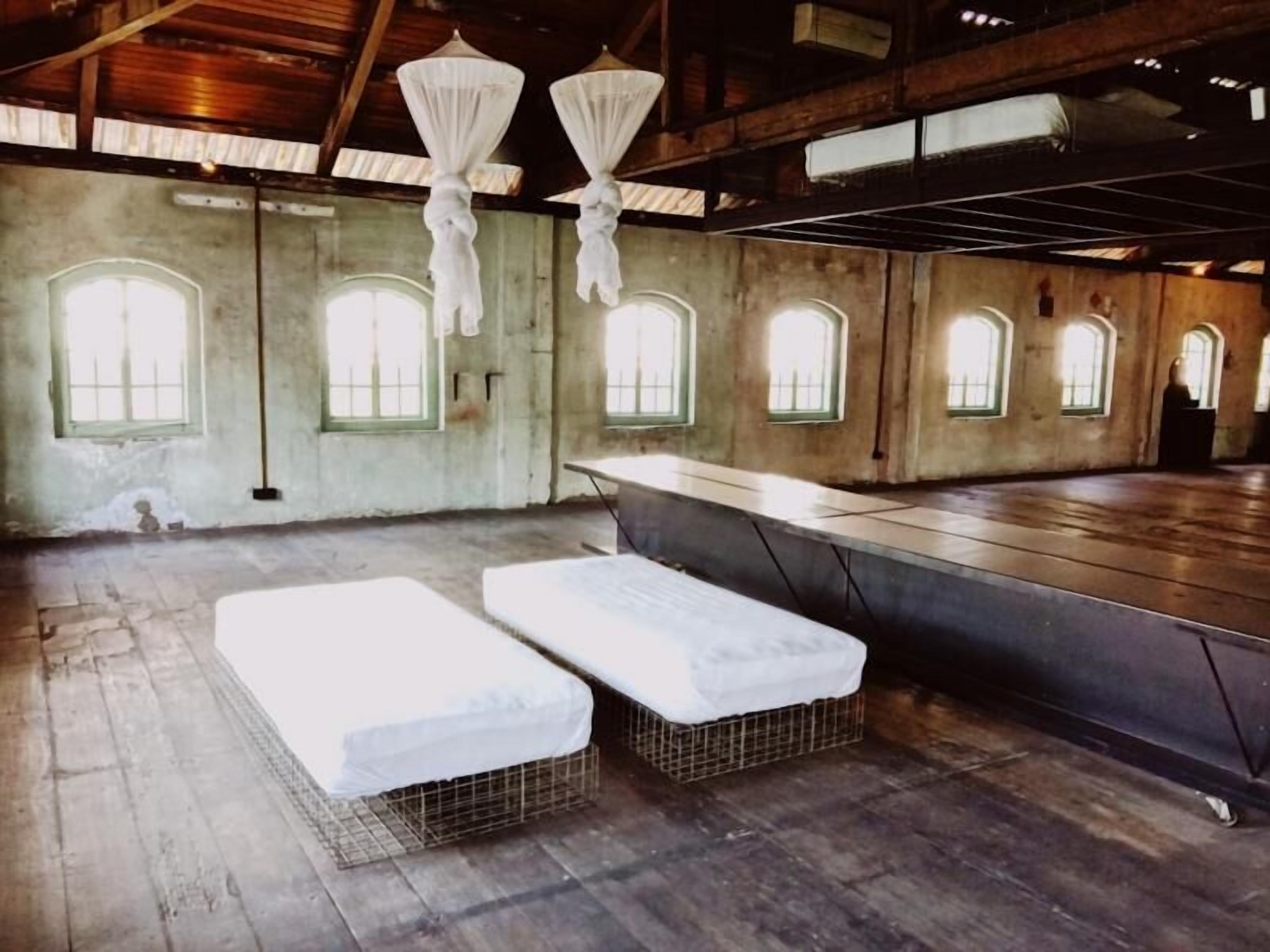 A room with two bunk beds, a long table, and multiple arched windows.