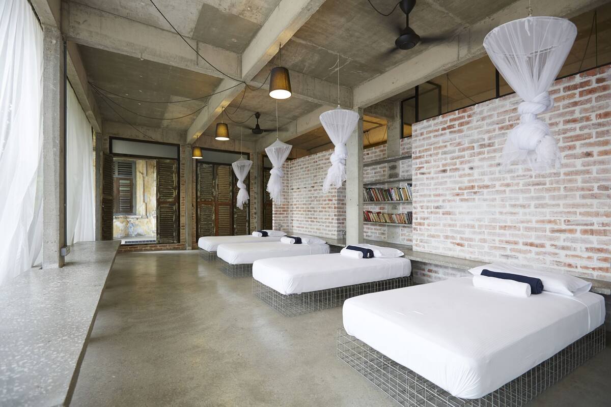 A hotel room with four beds, a brick wall, and hanging lights.
