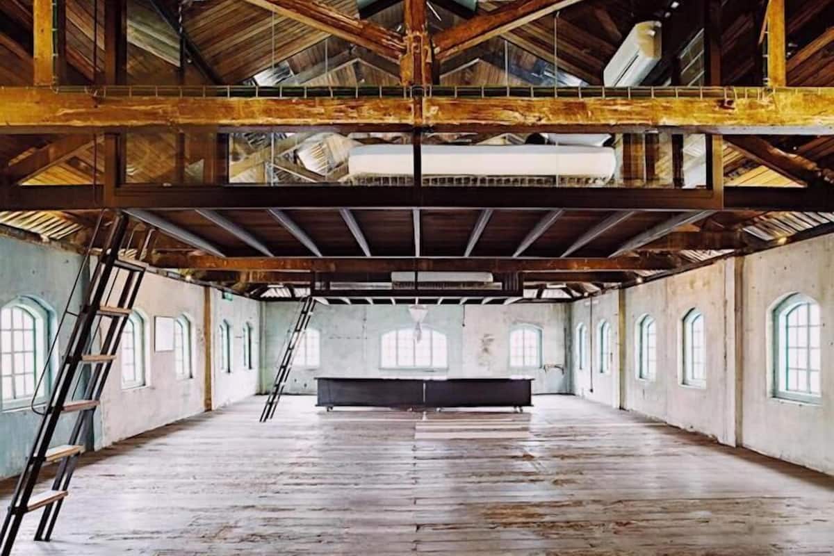 A large, open interior space with high ceilings and wooden beams, featuring a central staircase and multiple windows.