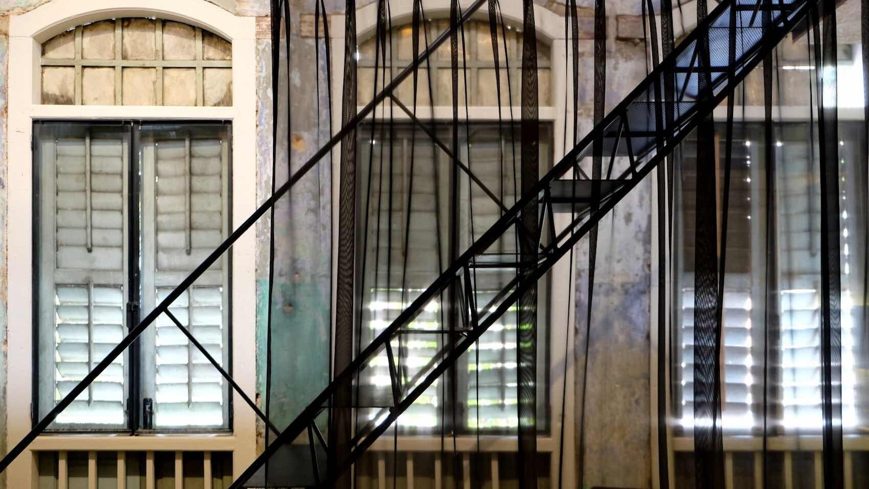 Un escalier avec des rampes en métal et des fenêtres équipées de stores.