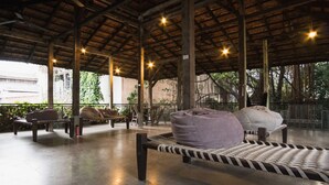 A covered outdoor seating area with benches and cushions, a concrete floor, and a wooden ceiling structure. - Belakang Kong Heng by DreamScape (Ipoh)