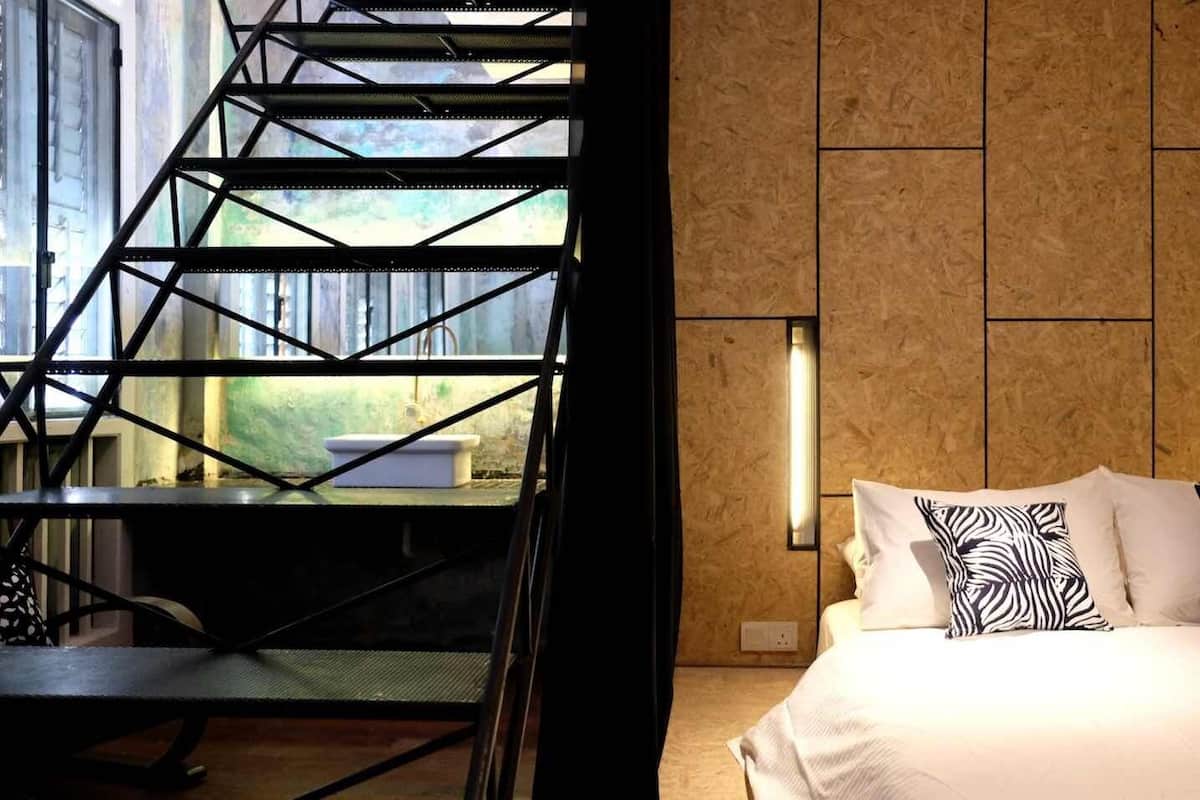 A modern hotel room with a bed, a staircase, and a view of a bathroom.
