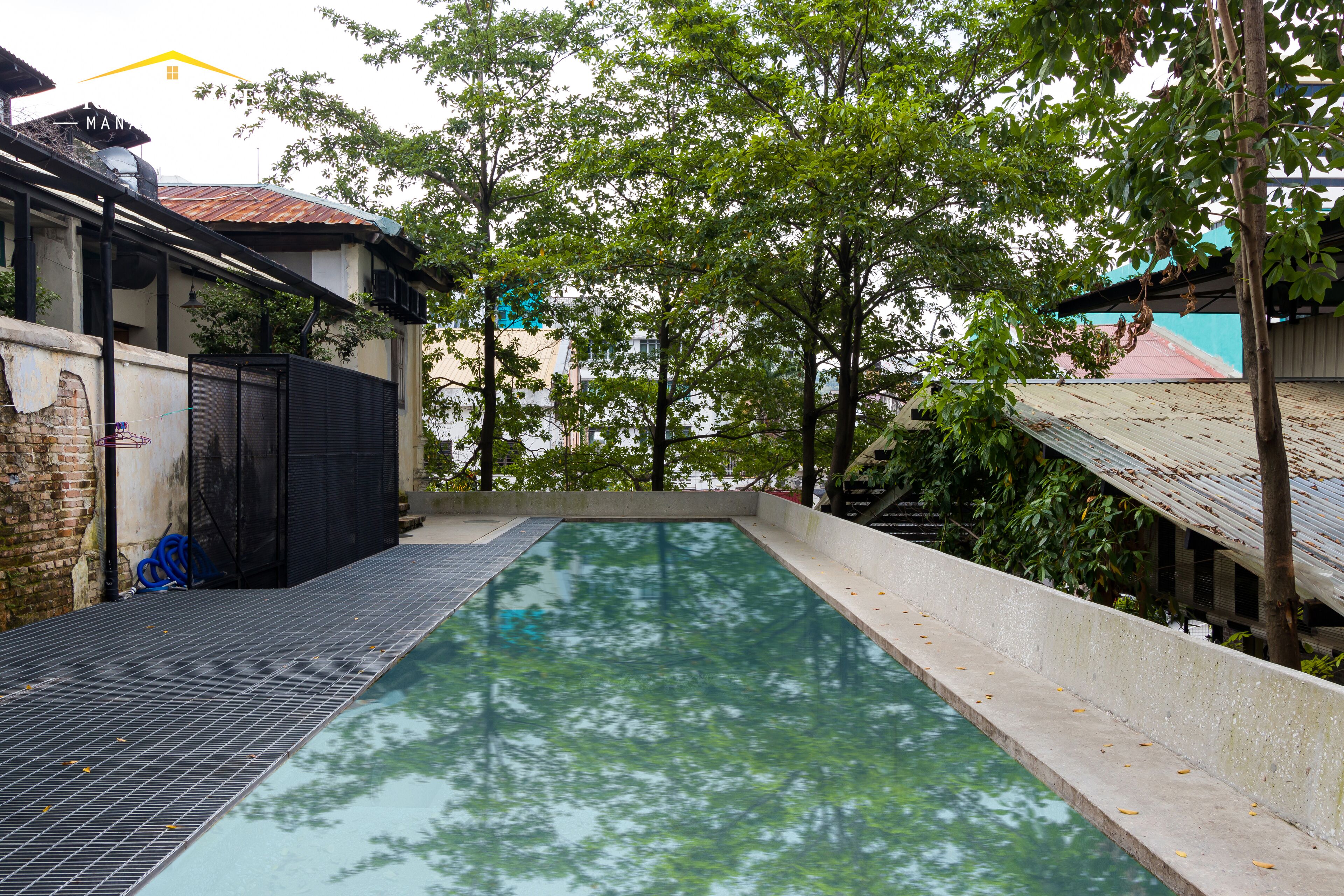 A swimming pool with a tiled deck, surrounded by trees and buildings.