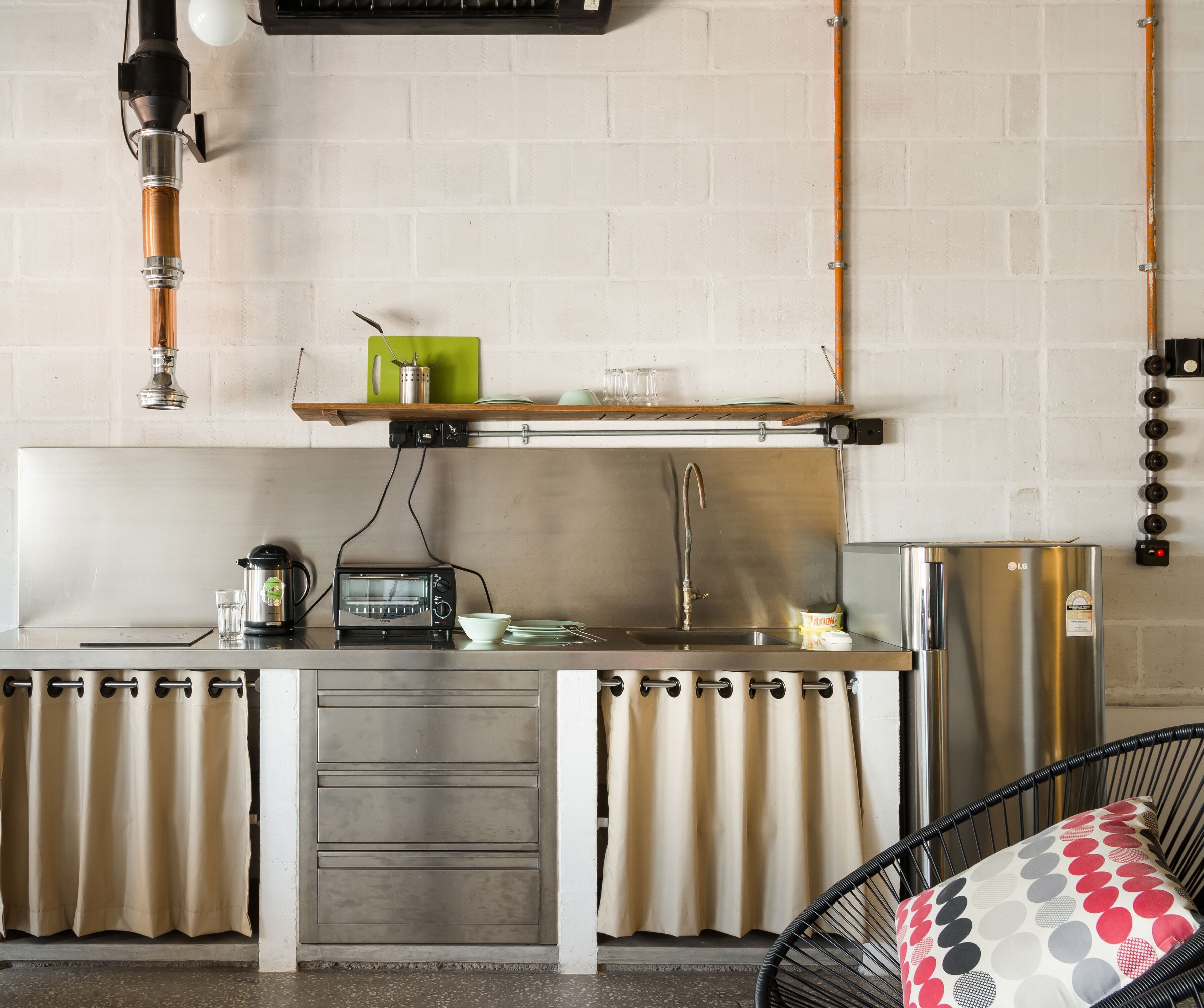 A kitchenette with a stove, toaster, sink, and a hanging pot rack.