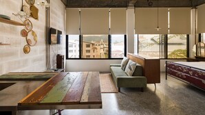 A modern interior with a wooden bench, a green sofa, and a view of buildings through large windows. - Belakang Kong Heng by DreamScape (Ipoh)