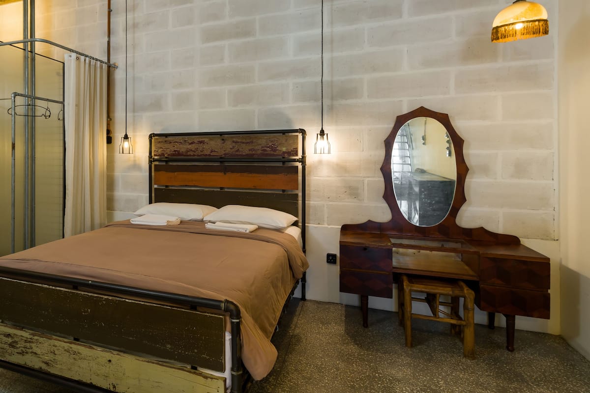 A bedroom with a bed, a wooden dresser, a mirror, and a hanging light fixture.