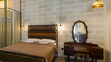 A bedroom with a bed, a wooden dresser, a mirror, and a hanging light fixture.