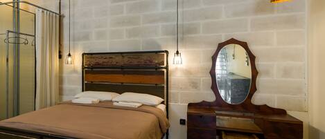 Une chambre à coucher avec un lit, une commode en bois, un miroir et un luminaire suspendu.