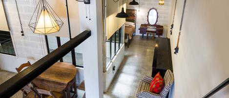 Un interior moderno con una mesa de comedor de madera, sillas, una lámpara colgante y una escalera que sube a un nivel superior.