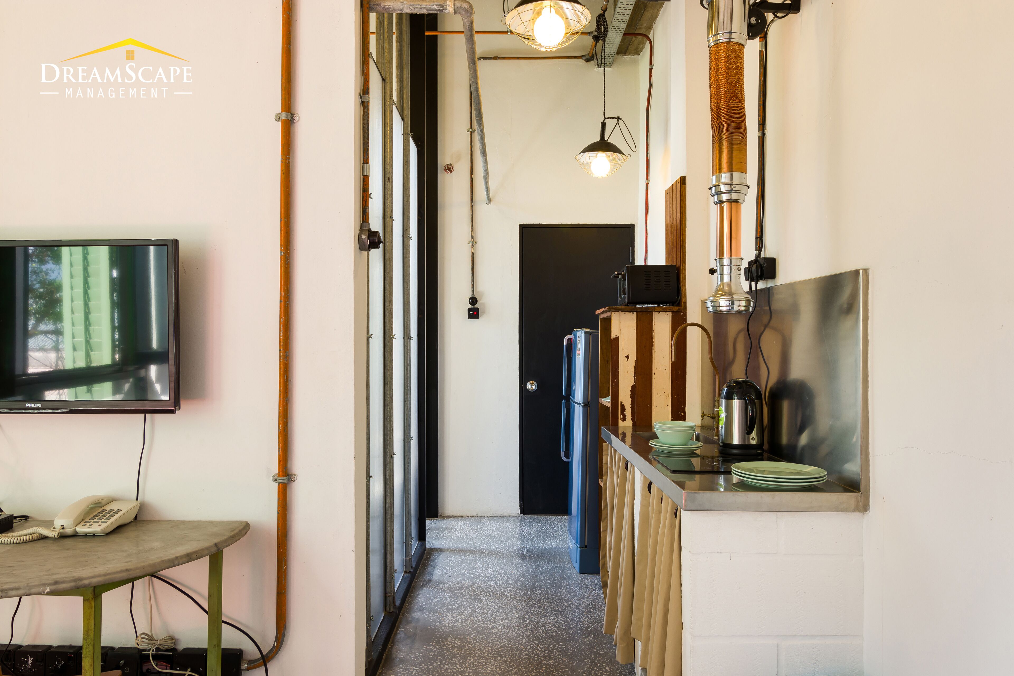 Un pasillo estrecho con un televisor a la izquierda, una mesa de madera y una zona de cocina a la derecha.