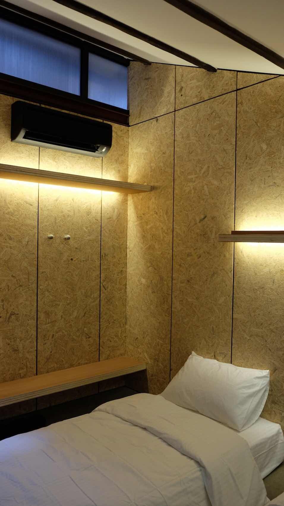 Une chambre à coucher comprenant un lit, une table de chevet, un climatiseur fixé au mur et une fenêtre avec des stores.