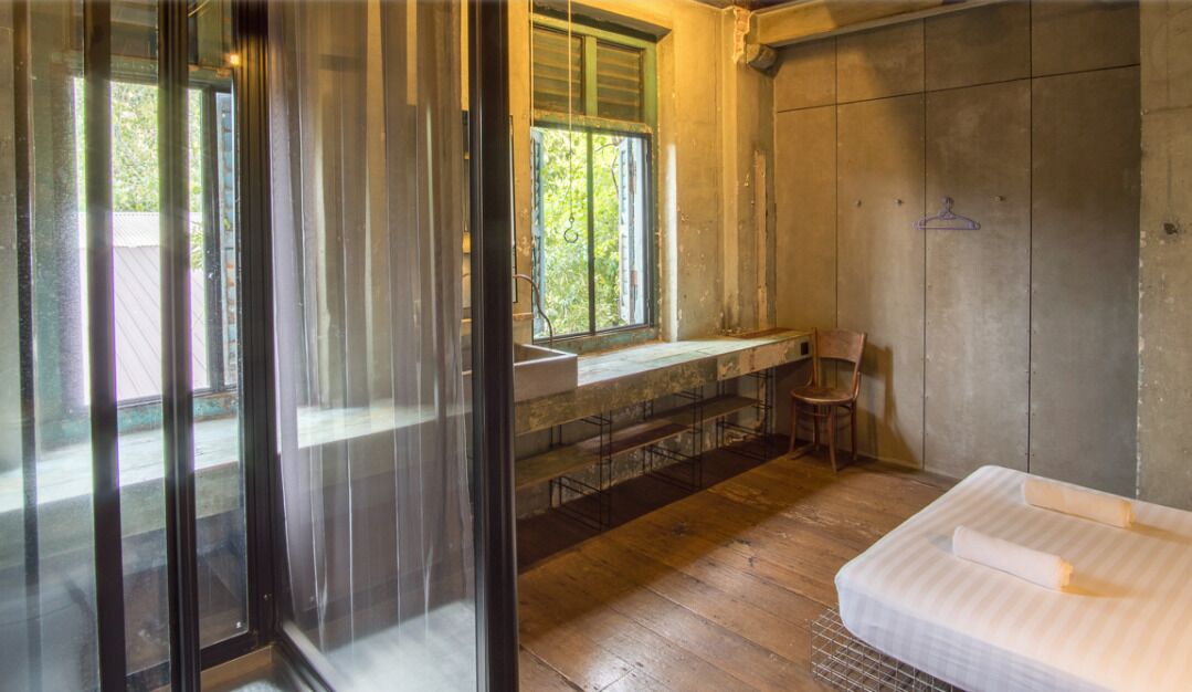 A bedroom with a large window, a wooden floor, a bed with white bedding, and a chair.