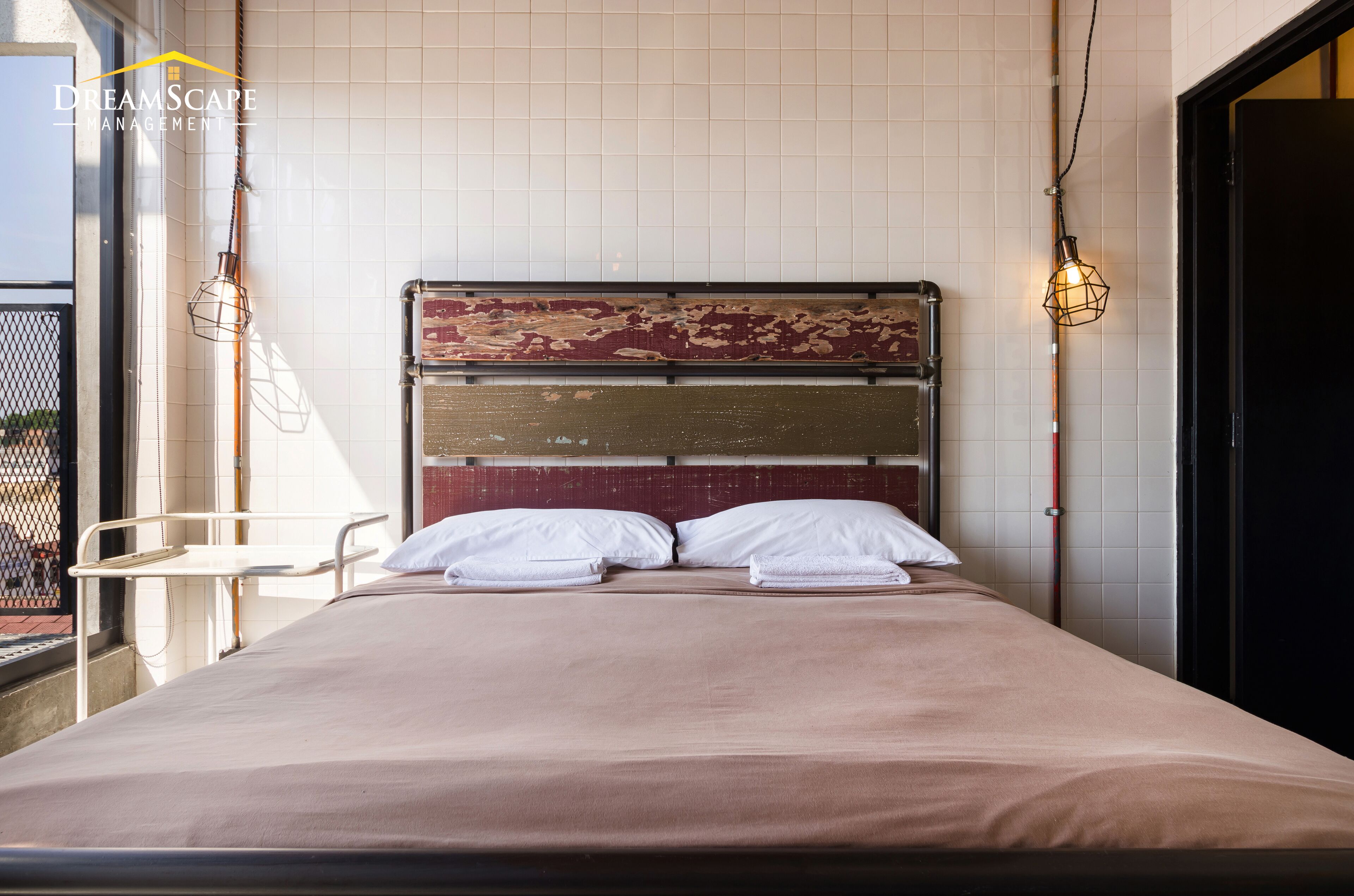 A hotel room with a bed, white pillows, a metal headboard, and a balcony with a chair.