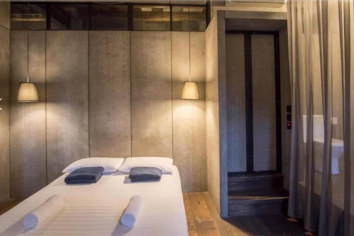 A hotel room with a bed, two wall-mounted lamps, a towel, and a door leading to a staircase.