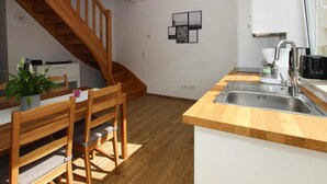 A kitchen with wooden flooring, a wooden dining table with chairs, a built-in sink, and a staircase leading to another level. - Reihenhaus in Malchow (Malchow)