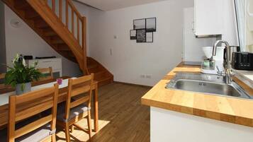 Una cucina con pavimento in legno, un tavolo da pranzo in legno con sedie, un lavello incassato e una scala che conduce a un altro piano.