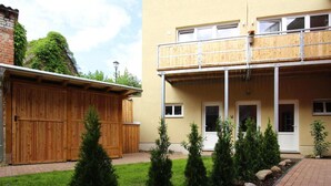 A two-story building with a wooden balcony, a brick wall, and a small garden with shrubs and rocks. - Reihenhaus in Malchow (Malchow)