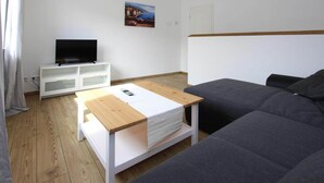 A modern living room with a grey sofa, a wooden coffee table, a TV on a white cabinet, and a painting on the wall. - Reihenhaus in Malchow (Malchow)