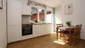 A kitchen with white cabinets, a wooden countertop, and a dining area with a table and chairs. - Reihenhaus in Malchow (Malchow)