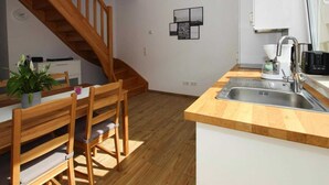 A modern kitchen with wooden flooring, a wooden dining table with chairs, a built-in sink, and a staircase leading to another room. - Reihenhaus in Malchow (Malchow)