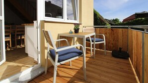 A wooden deck with a table and chairs, a window, and a door leading to an interior space. - Reihenhaus in Malchow (Malchow)
