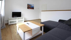 A modern living room with a grey sofa, a wooden coffee table, a white TV stand, and a painting on the wall. - Reihenhaus in Malchow (Malchow)