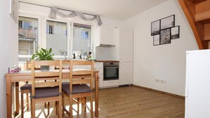 A modern kitchen with white cabinets, a wooden dining table, and chairs. There is a window with curtains, a built-in oven, and a small balcony visible through the window. - Reihenhaus in Malchow (Malchow)