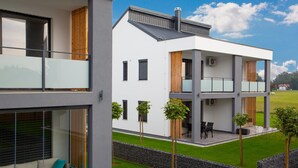 A modern two-story building with a balcony, a small outdoor seating area, and a well-maintained lawn. - Apartments Banonia - Morning Dawn (Verzej)