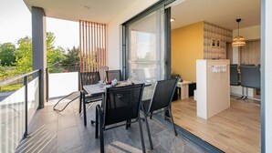 A modern dining area with a table and chairs, a kitchen area with a dining table and chairs, and a balcony with a railing. - Apartments Banonia - Morning Dawn (Verzej)