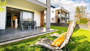Ein modernes, zweistöckiges Haus mit Terrasse, Essbereich und Liegestuhl.