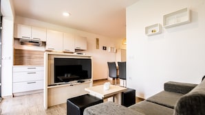 Een moderne keuken met witte kasten, een inbouwoven en een flatscreen televisie. Er is een eethoek met een tafel en twee stoelen.