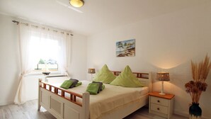 A bedroom with a bed, bedside tables, a window with curtains, a lamp, and a vase with dried plants. - Zur Alten Boddenfischerei (Saal)