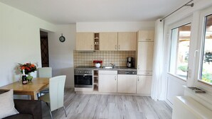 A compact kitchen with modern appliances, a dining area with a table and chairs, and a large window providing natural light. - Zur Alten Boddenfischerei (Saal)