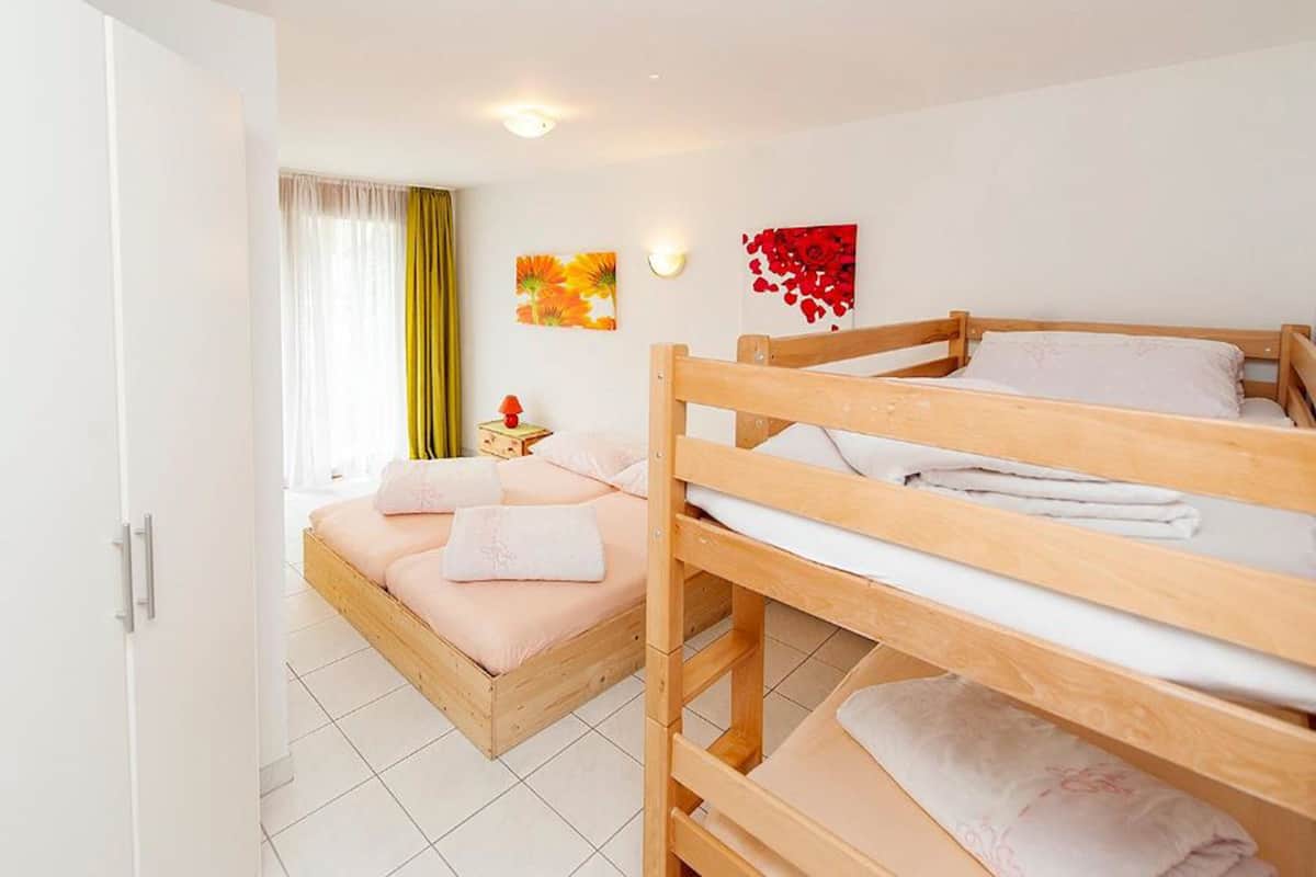 A bedroom with two bunk beds, a bedside table with a lamp, and a window with curtains.