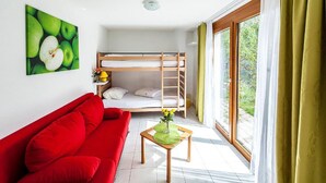 A room with a bunk bed, a red sofa, a small table with a vase, and a large window with curtains. - Hotel Cuntera (Medel)