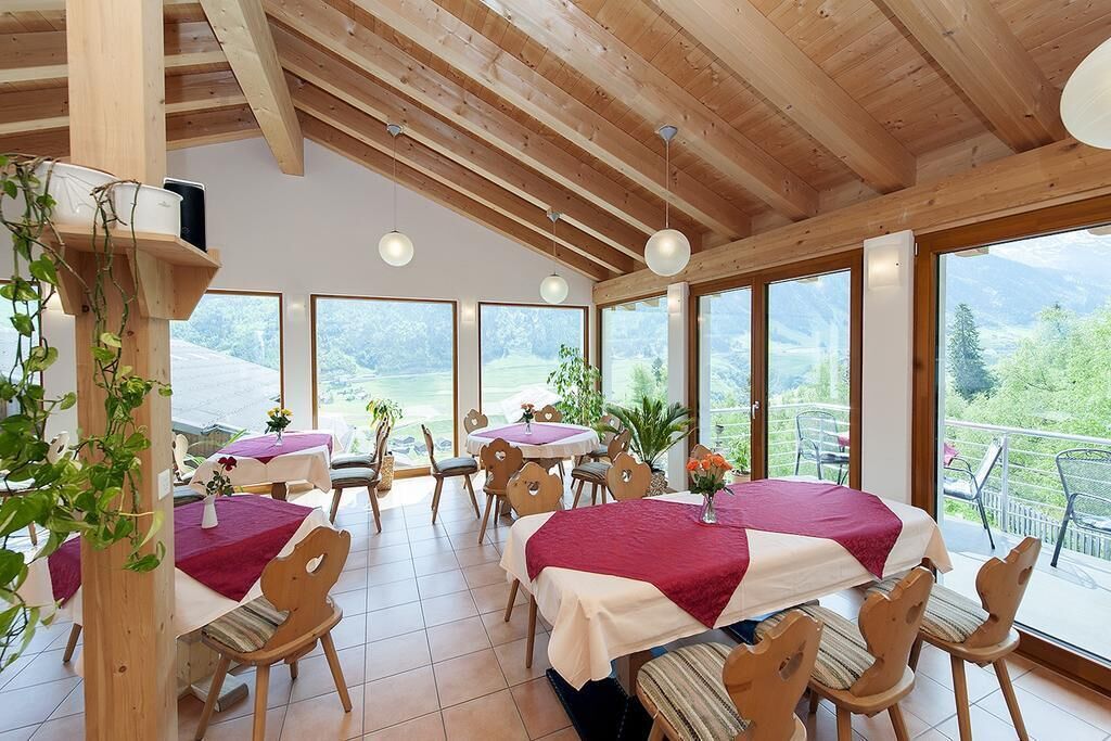 Un comedor con mesas y sillas de madera, ventanas amplias con vistas a la vegetación y un alto techo de madera.