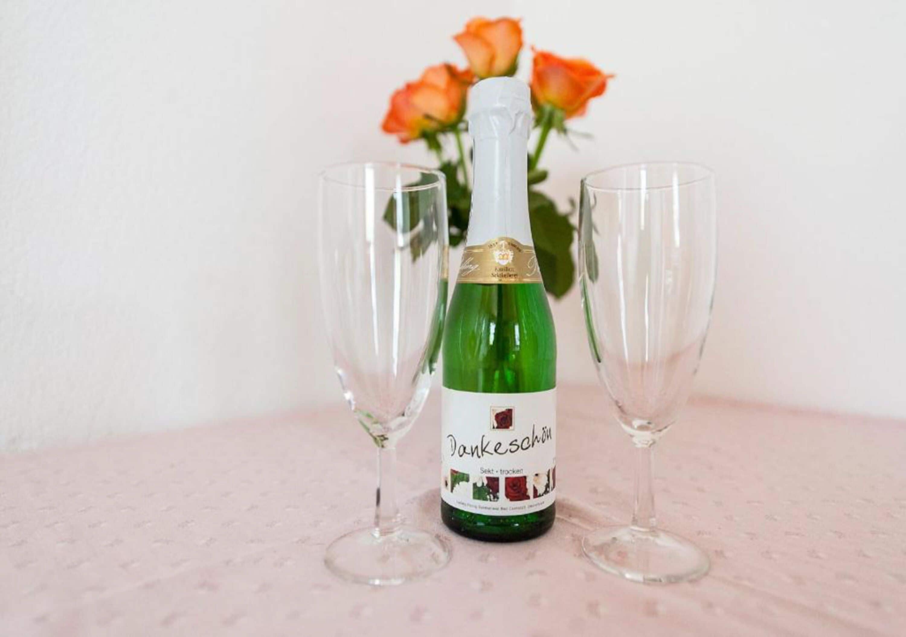 Une bouteille de vin, deux verres vides et un bouquet de roses en arrière-plan.