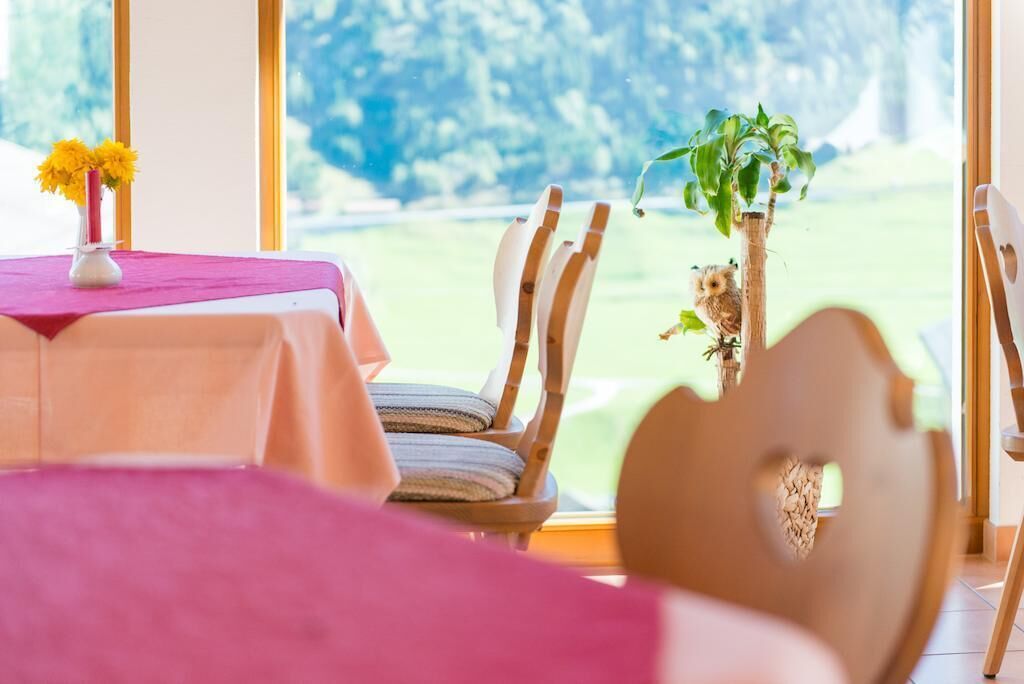 Un comedor con una mesa lista para dos, sillas y vistas a un jardín a través de grandes ventanales.