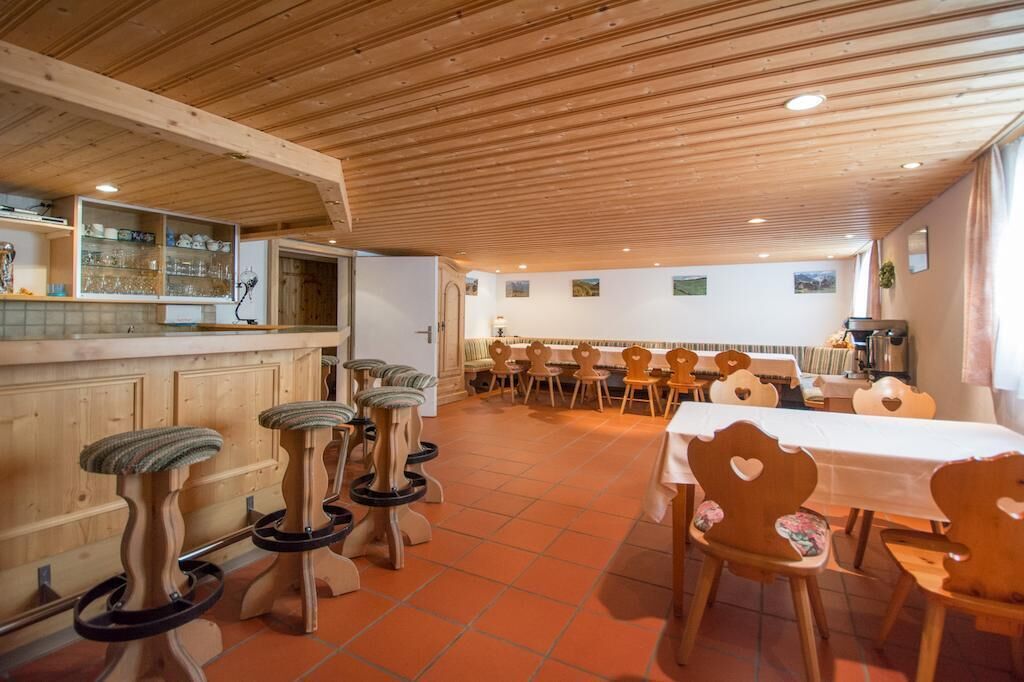 Un comedor con sillas y taburetes de madera, una mesa larga y una zona de bar con estanterías.