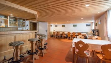 Un comedor con sillas y taburetes de madera, una mesa larga y una zona de bar con estanterías.