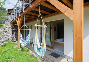 Una estructura de madera con un balcón, un muro de piedra y dos hamacas colgadas del techo.
