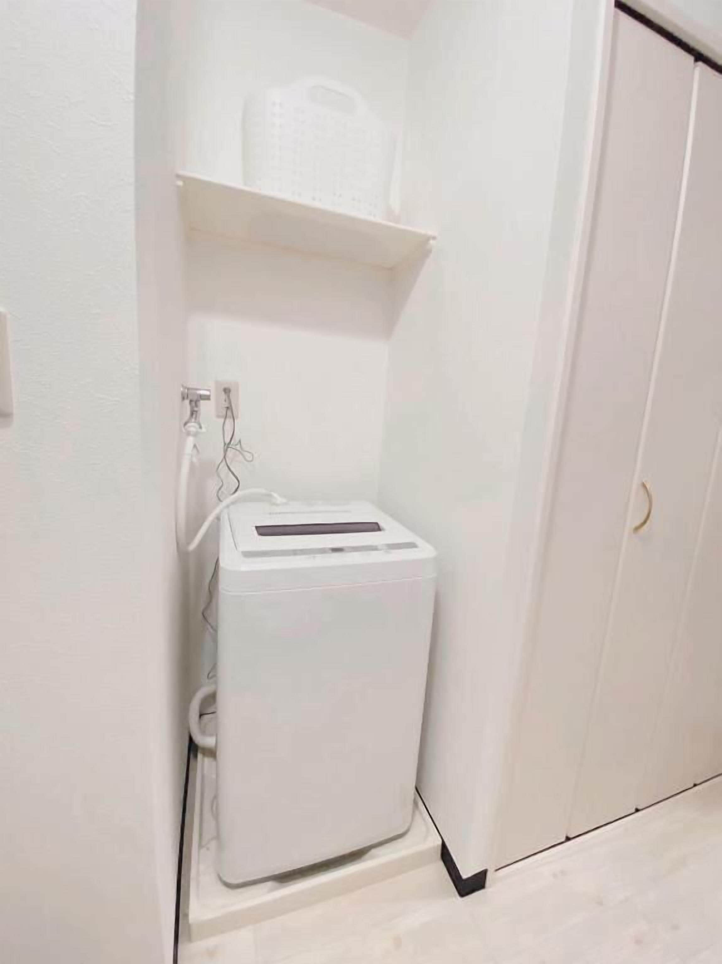 A compact, white utility room with a small white appliance, possibly a water heater, on a shelf.